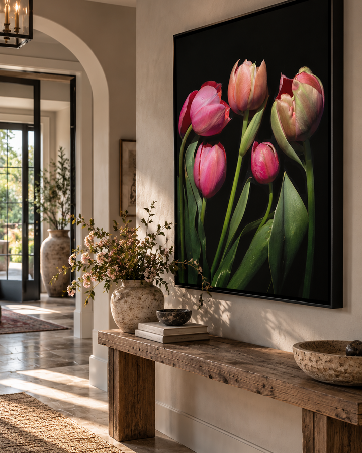 A large framed wall art print - A Fine Romance - featuring pink tulips on a black background, displayed in a styled interior hallway above a rustic wooden bench.