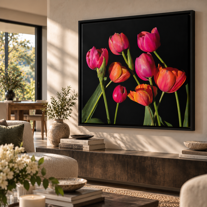 A framed wall art print featuring a cluster of bright pink, red, and orange tulips on a black background, displayed in a modern living room setting.