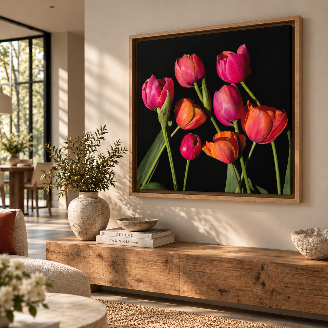 A framed wall art print featuring a cluster of bright pink, orange, and magenta tulips on a black background, displayed above a wooden console in a modern living room setting.