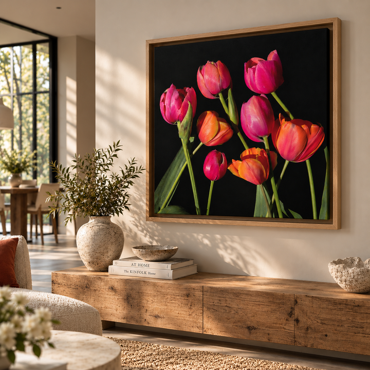 A framed wall art print featuring a cluster of bright pink, orange, and magenta tulips on a black background, displayed above a wooden console in a modern living room setting.