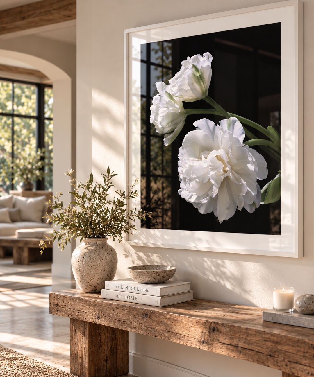 A large framed wall art print featuring white Tulip flowers against a black background, displayed in a white frame on a beige wall above a rustic wooden console table in a styled living room.