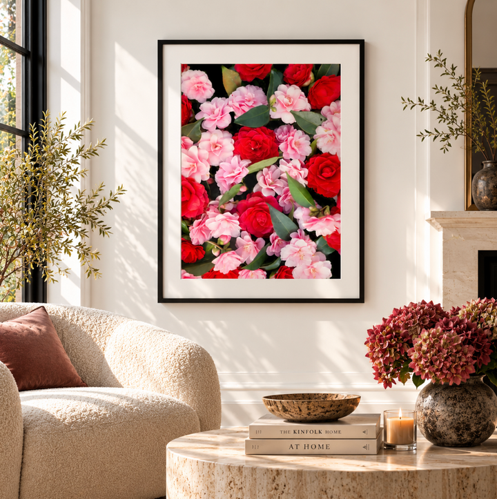 Front view of a red and pink camellia print in a black frame with a white border beside a fireplace.