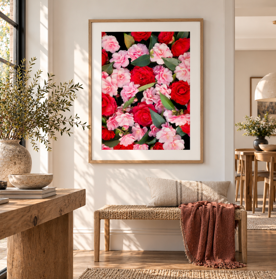Front view of a red and pink camellia print in a natural timber frame with a white border above a woven bench.