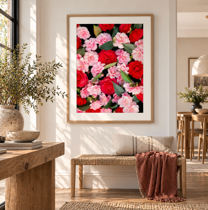 Front view of a red and pink camellia print in a natural timber frame with a white border above a woven bench.