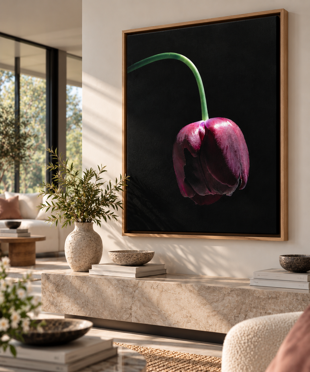 A framed wall art print featuring a single dark burgundy tulip with a green stem on a black background, displayed in a modern living room setting.